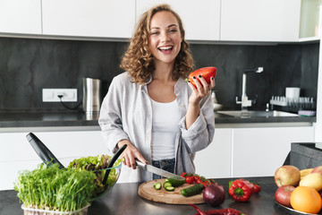 Happy young woman making a salad at the kitchen