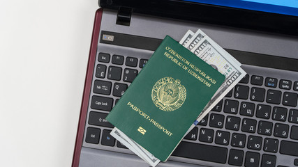 Fototapeta premium Passport of Uzbekistan with US dollars on laptop keyboard. Online registration. Concept - briber and corruption. Top view
