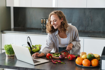 Happy young woman making a salad at the kitchen