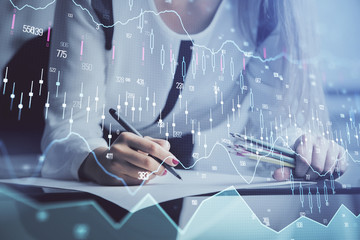 Double exposure of hands making notes with forex chart huds. Stock market concept.