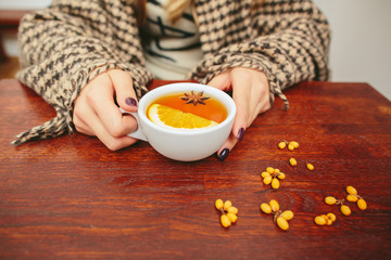 Girl holds a cup of tea in her hands and is wrapped in a plaid