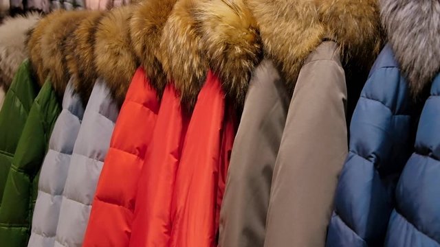 Close up of set of down jackets with hood on a clothes rack. Sale shopping concept.