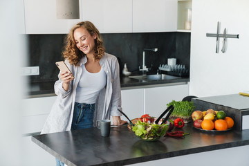 Smiling young woman using smartphone in kitchen