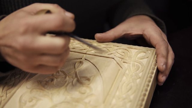 Hand-carved wood close-up. Unrecognizable craftsman carving wooden ornament on backgammon. Carpenter chiseling, shaping and sanding wood work for carved decoration