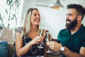 Beautiful young couple is holding glasses of champagne and smiling while celebrating at home