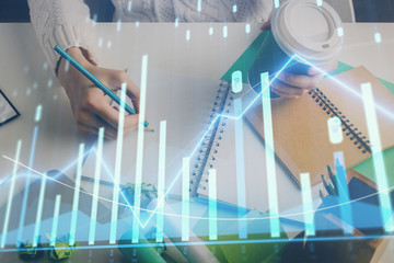 Financial forex graph displayed on hands taking notes background. Concept of research. Multi exposure