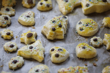 Selbstgemachte Weihnachtsplätzchen mit Zutaten, Zuckerstreusel, Schokolade auf Backblech an Weihnachten als top view Detail.