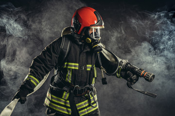 brave extinguisher or fireman dressed in dark protective suit uniform, with helmet on head, using ropes, hammer and other special equipment at work