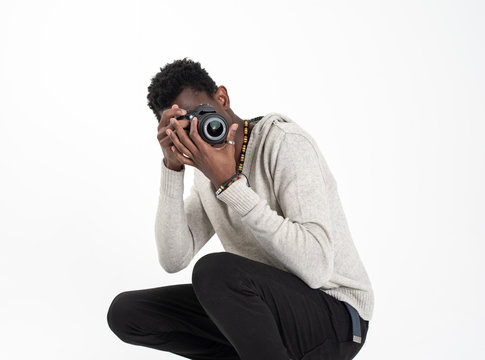 A black skin male photographer in a gray sweater and black pants is making photos with his black camera