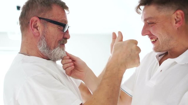 Elderly father is pleased to see his adult son. Two men are smiling, hugging and looking at each other. Good relationship, happy family