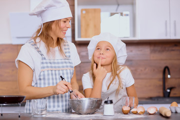 caucasian mother and daughter bake together, make dough and use ingredients need for it. Happy teamwork in kitchen of woman and her child