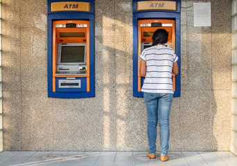 A woman using automated teller machine. Young woman is withdrawing money from ATM on the street.