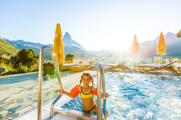 Kids play in outdoor infinity swimming pool of luxury spa alpine resort at sunset in Alps...