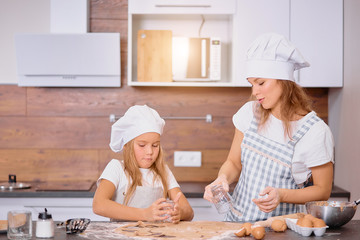 caucasian woman and child girl together in kitchen, woman teach kid girl to bake and cook, wearing aprons. generations and family concept