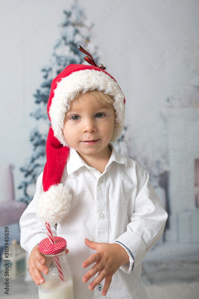 Sticker Beautiful toddler boy with red santa hat, holding bottle with milk, drinking