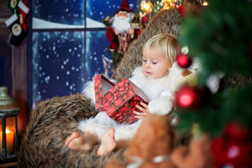 Blond toddler child, boy, opening present at home, sitting in cozy sofa