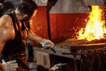 caucasian young strong blacksmith working with open fire in furnace. The blacksmith forging hot iron in workshop