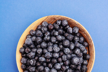 Bowl of blueberries in wooden bowl over blue background isolated. Fresh berry.