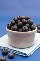 Blueberries in white bowl over blue background, fresh berry over blue background.