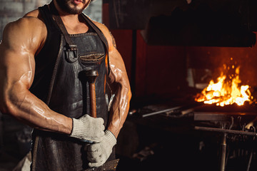 cropped strong muscular male blacksmith holding handmade metal for manufacturing, wearing leather...
