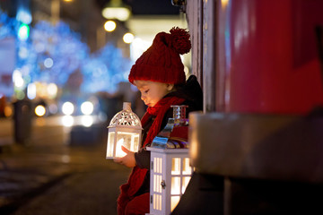 Sweet little toddler boy, holding lantern and a teddy bear at night in Prague