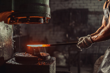 young bearded man in leather uniform heats the metal on fire isolated in workshop