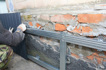 Brick House foundation wall repair,  renovation  with builder hands installing metal sheets for...