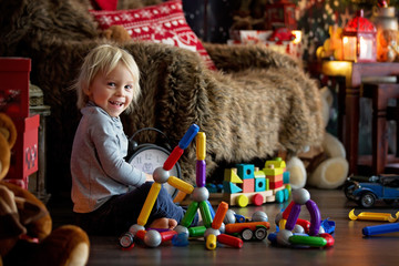Sweet blonde toddler boy, playing with plastic construction, making different shapes © Tomsickova