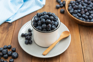 Ripe blueberries in metalic cup on the wooden table. Fresh berries for breakfast. Copy space.