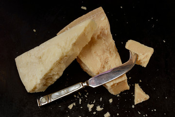 Piece of parmesan cheese with cheese knife on dark background,  front view
