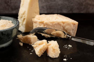 Piece of parmesan cheese with cheese knife on dark background,  front view