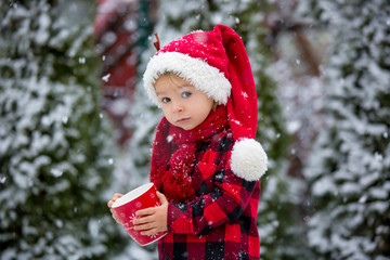 Sweet beautiful toddler boy, holding cup with hot milk, drinking outdoor in the snow, enjoying winter