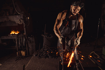 young muscular blacksmith man manually forging the molten metal. Blacksmith hammering hot metal arrow blade, wearing leather apron