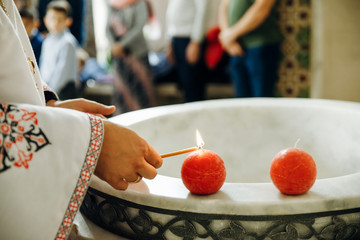 Orthodox priest lights candles near font for baptism