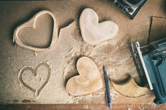 top view of carpenter workplace close-up, wooden blanks in shape of heart, sawdust and carpentry tools, flatlay