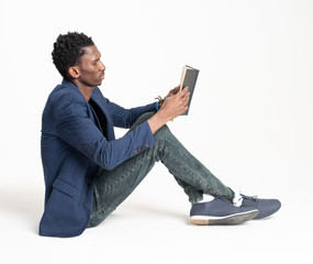 A black skin guy (man) in a blue jacket and jeans is sitting with a book like a student reading