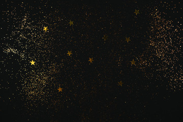 Fototapeta na wymiar Golden sparkles and stars on black backdrop. Holiday concept.