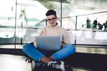 Young male looking at camera with legs crossed and laptop on knees