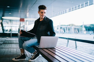 Smiling young man with notebook on knees working on laptop