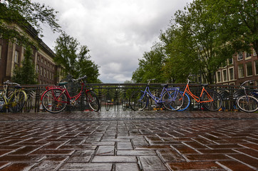 Fototapeta na wymiar Amsterdam, Holland, August 2019. Typical view over a canal in the historic center. Rainy day. Colorful bikes parked on the railing.