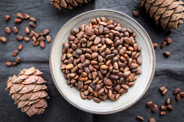 Cedar or pine nuts in a bowl with cones on gray background, top view