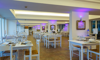 Fototapeta na wymiar evening interior of the restaurant with white furniture and tables in resort European hotel, Greece