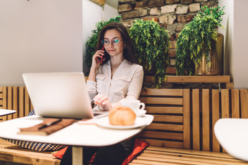 Professional businesswoman using laptop and talking on mobile phone at cafe