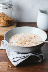 Baked granola and almond milk in a ceramic bowl on breakfast table.