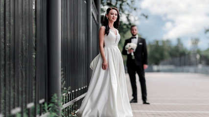 happy bride in wedding dress standing on city street