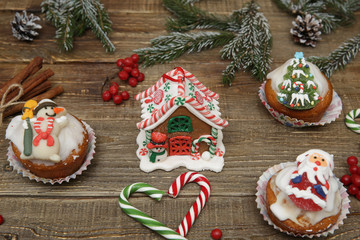 Christmas cupcakes, gingerbread house and muffin with Santa Claus, snowman, green spruce and candy cane on wooden background, Christmas composition. Holidays and Christmas concept. 