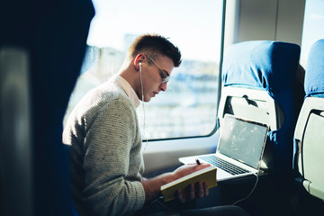 Freelance young handsome man writing notes while riding in train