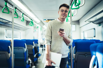 Fototapeta na wymiar Cheerful man with smartphone standing in train