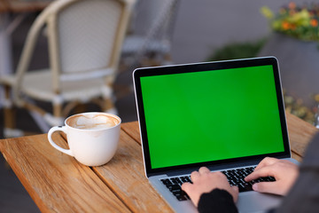 over shoulder of people using green screen laptop computer on wooden table. with a cup of coffee. blur background