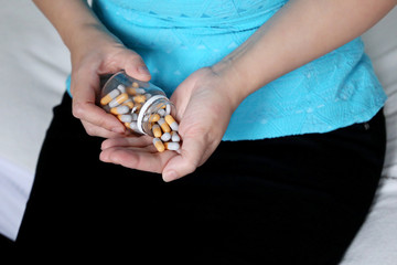 Woman with pills sitting on a bed, female hands with bottle of capsules. Concept of vitamins for beauty, diet pill, contraceptive, medication for stomach or sleeping pill